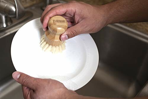 Person cleaning a dish with a bamboo brush over a sink.