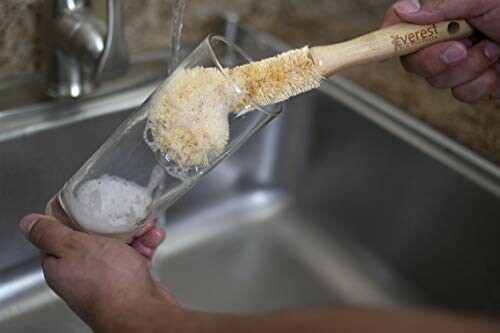 Person cleaning a glass with a brush over a sink.