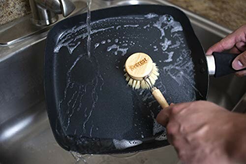 Person cleaning a pan with a brush under running water.