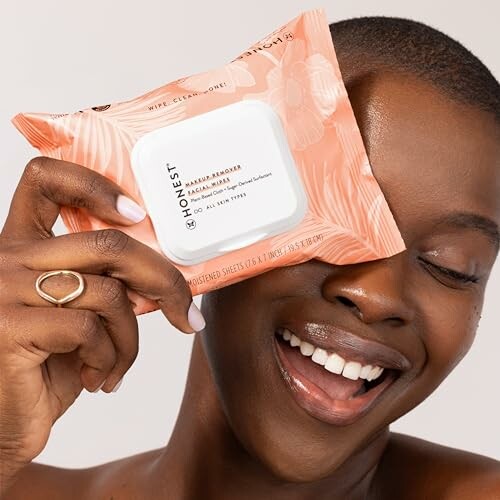 Smiling woman holding makeup remover wipes near her face.